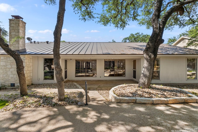 exterior space with a standing seam roof, a chimney, and metal roof