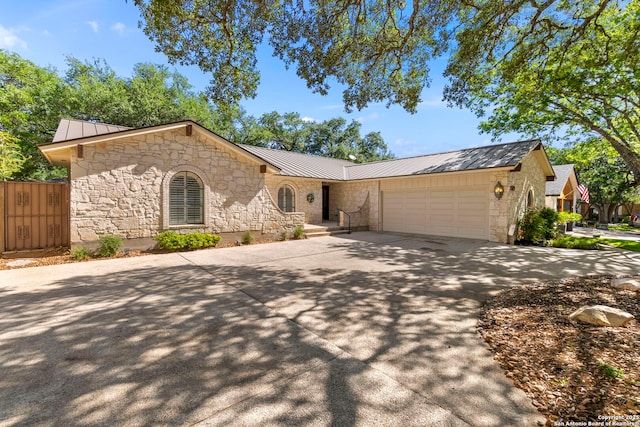 single story home with a garage, concrete driveway, stone siding, metal roof, and a standing seam roof