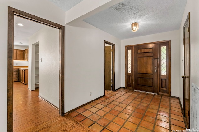 foyer with a textured ceiling, baseboards, and visible vents