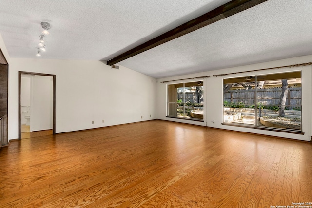 spare room featuring wood finished floors, a textured ceiling, vaulted ceiling with beams, and visible vents