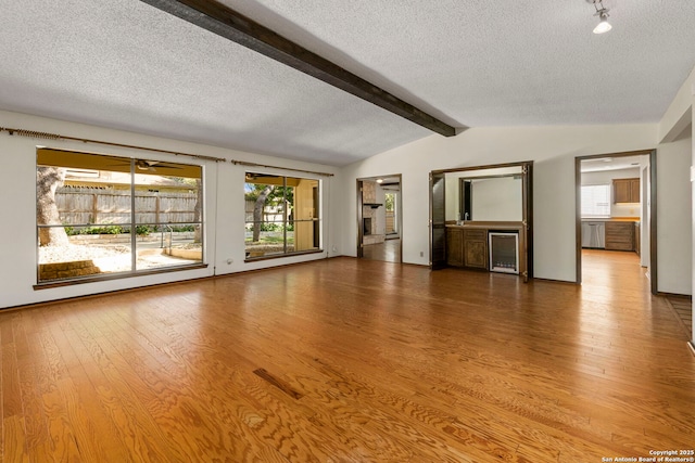 unfurnished living room with beverage cooler, a textured ceiling, lofted ceiling with beams, and wood finished floors