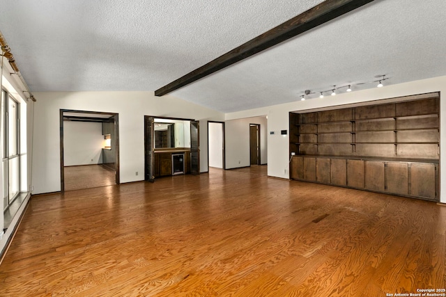 unfurnished living room with wood finished floors, a textured ceiling, vaulted ceiling with beams, and baseboards