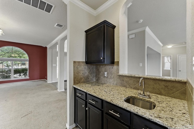 kitchen featuring visible vents, a sink, ornamental molding, and light stone counters