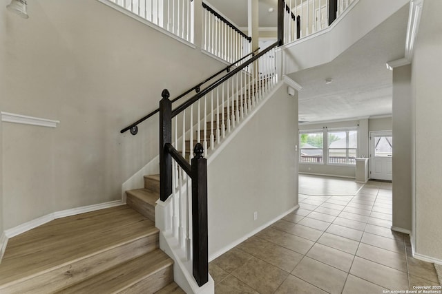 stairs featuring baseboards, ornamental molding, tile patterned flooring, and a towering ceiling