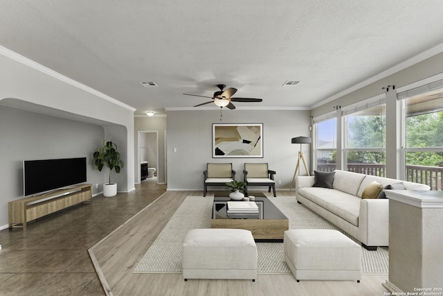 living area featuring ceiling fan, baseboards, crown molding, and visible vents