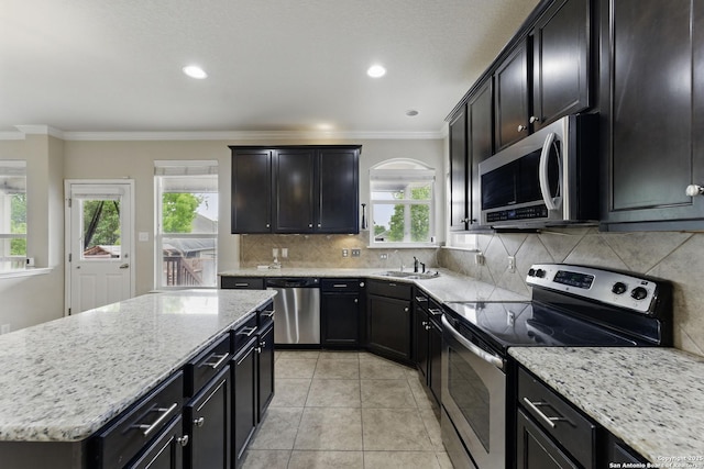 kitchen with light stone counters, stainless steel appliances, backsplash, a kitchen island, and crown molding