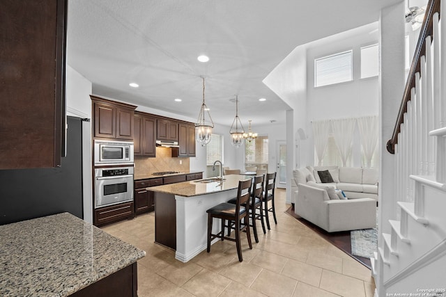 kitchen with stainless steel appliances, open floor plan, a chandelier, a kitchen bar, and under cabinet range hood