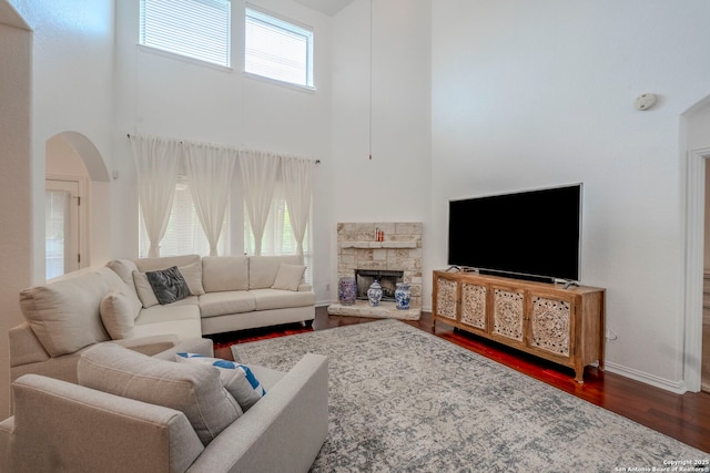 living room with baseboards, a high ceiling, arched walkways, and dark wood-style floors