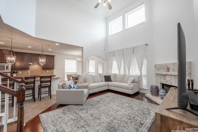 living area featuring recessed lighting, ceiling fan with notable chandelier, wood finished floors, a high ceiling, and a fireplace
