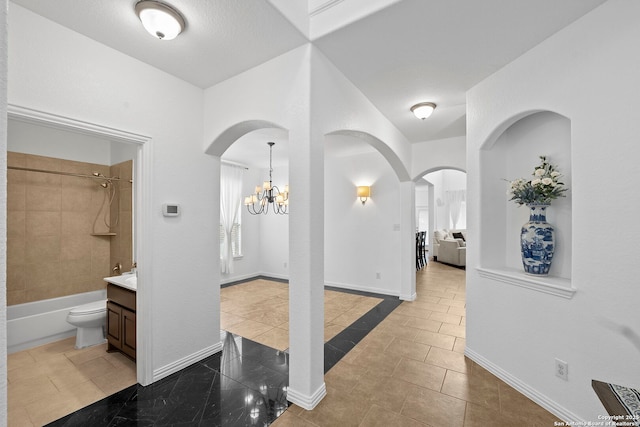 interior space featuring tile patterned floors, baseboards, arched walkways, and a notable chandelier