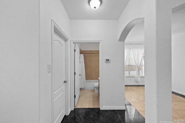 hallway featuring arched walkways, tile patterned flooring, and baseboards