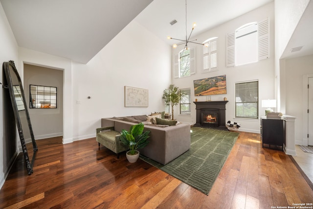 living area featuring high vaulted ceiling, hardwood / wood-style flooring, a warm lit fireplace, a chandelier, and baseboards