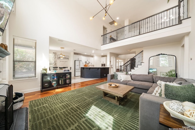 living area with a towering ceiling, a chandelier, light wood-style floors, and stairs