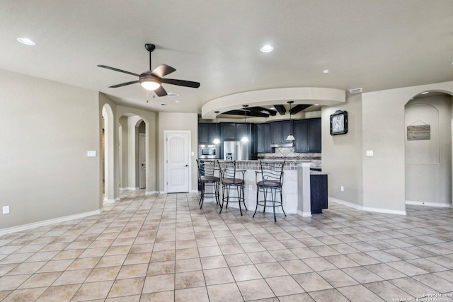 kitchen with a ceiling fan, tasteful backsplash, arched walkways, stainless steel appliances, and a kitchen bar