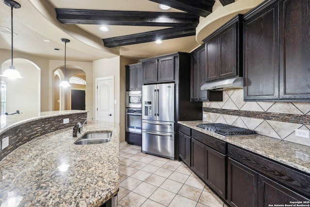 kitchen featuring a sink, arched walkways, appliances with stainless steel finishes, backsplash, and under cabinet range hood