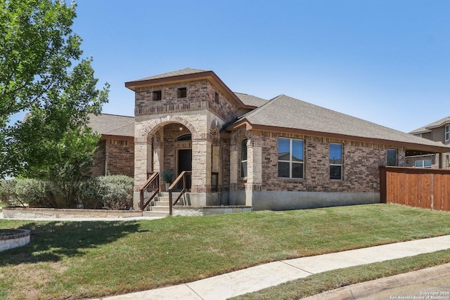 view of front of home with fence, a front lawn, brick siding, and roof with shingles