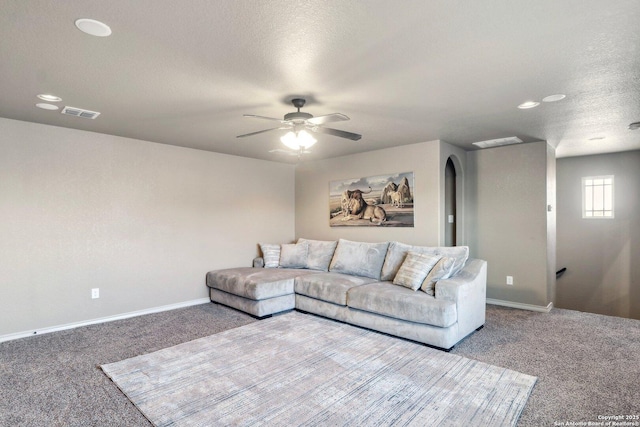 carpeted living room featuring a ceiling fan, a textured ceiling, arched walkways, baseboards, and visible vents