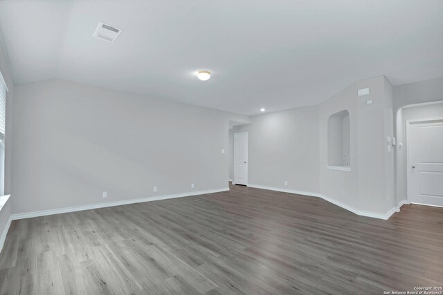 unfurnished room with wood finished floors, visible vents, lofted ceiling, and baseboards
