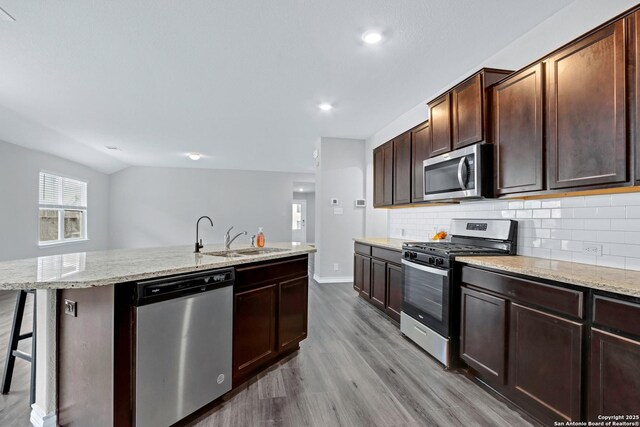 kitchen with light stone counters, a sink, decorative backsplash, stainless steel appliances, and dark wood finished floors