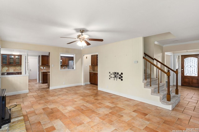 unfurnished living room featuring stairway, stone finish flooring, crown molding, baseboards, and ceiling fan