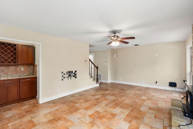 unfurnished living room featuring stone finish flooring, a ceiling fan, stairs, and visible vents