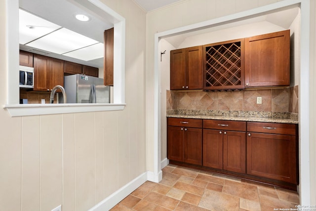 bar featuring decorative backsplash, baseboards, freestanding refrigerator, and a bar