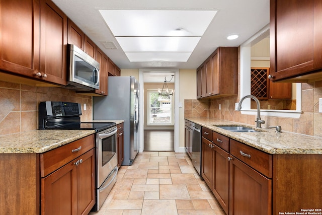 kitchen featuring tasteful backsplash, light stone countertops, stainless steel appliances, and a sink