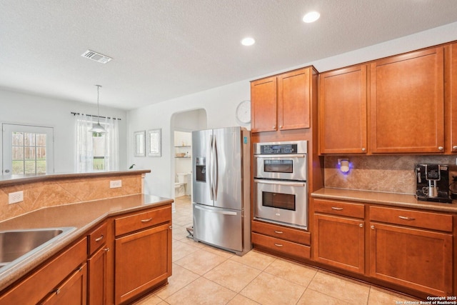 kitchen with stainless steel appliances, light tile patterned flooring, brown cabinetry, and tasteful backsplash