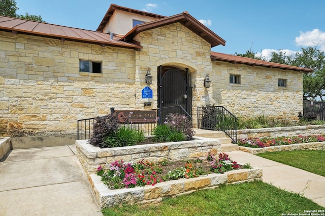doorway to property with a standing seam roof, fence, and stone siding