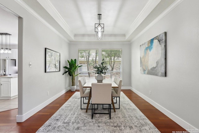 dining space with baseboards, dark wood-style floors, a raised ceiling, and crown molding