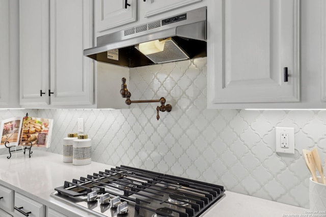 kitchen with under cabinet range hood, light countertops, backsplash, stainless steel gas cooktop, and white cabinetry