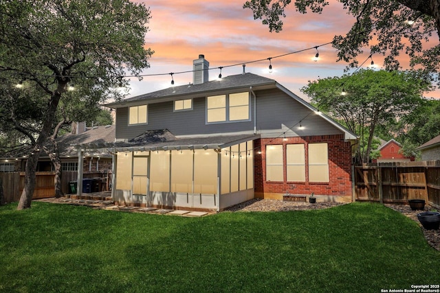 rear view of house featuring brick siding, a yard, a fenced backyard, and a chimney