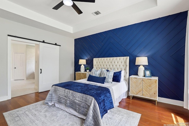 bedroom featuring a barn door, baseboards, wood finished floors, and visible vents
