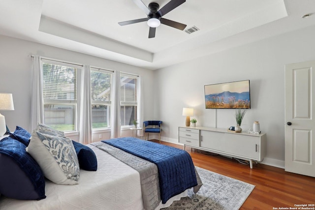 bedroom featuring a ceiling fan, wood finished floors, a raised ceiling, baseboards, and visible vents