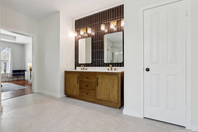 bathroom with a sink, double vanity, tile walls, baseboards, and walk in shower