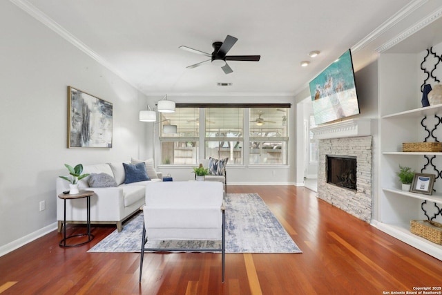 living room featuring wood finished floors, visible vents, crown molding, a fireplace, and ceiling fan