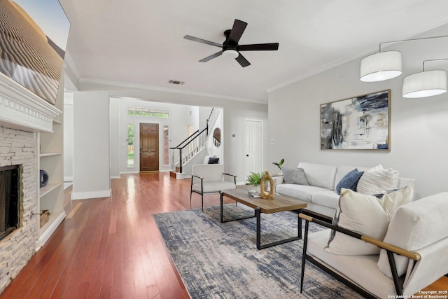 living room with stairway, a ceiling fan, a stone fireplace, hardwood / wood-style flooring, and ornamental molding