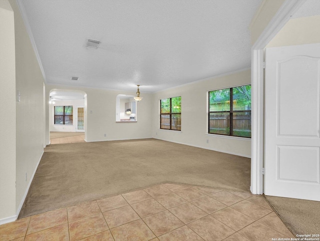 unfurnished living room with light tile patterned floors, visible vents, light colored carpet, and crown molding