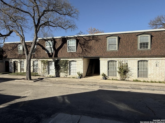 view of front of house featuring brick siding, a shingled roof, and mansard roof