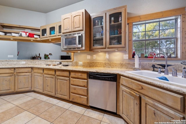 kitchen with light stone counters, light tile patterned floors, a sink, glass insert cabinets, and appliances with stainless steel finishes