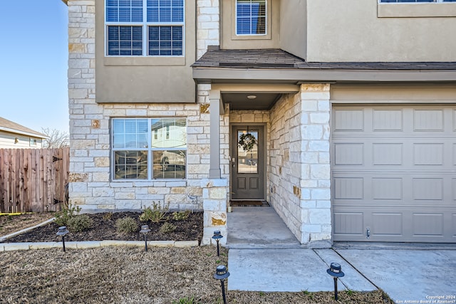 entrance to property with an attached garage, stone siding, and fence