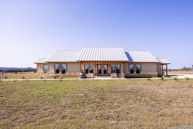 rear view of house featuring stone siding, a lawn, french doors, and metal roof