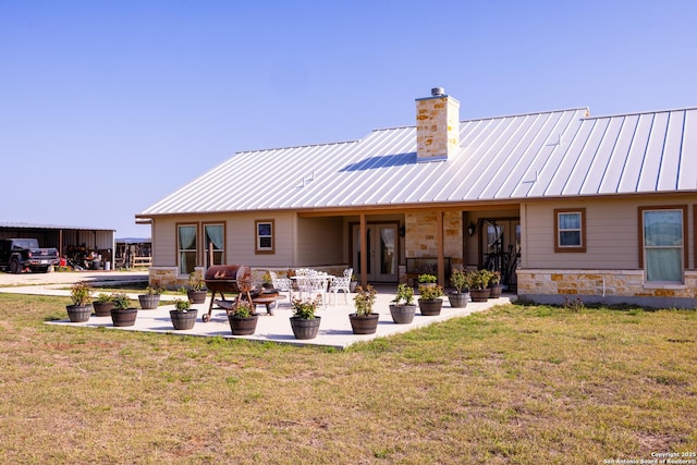back of property featuring a chimney, stone siding, a standing seam roof, and a yard