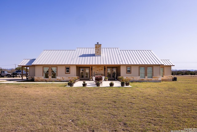 rear view of property with french doors, a lawn, stone siding, and metal roof