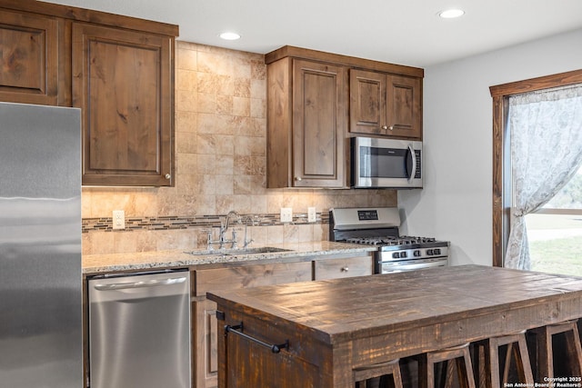 kitchen featuring stainless steel appliances, a sink, tasteful backsplash, recessed lighting, and light stone countertops