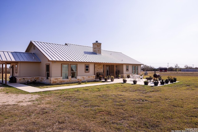 back of property featuring stone siding, a lawn, a chimney, and a standing seam roof
