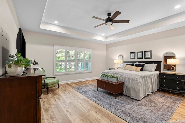 bedroom with light wood finished floors, a tray ceiling, and recessed lighting