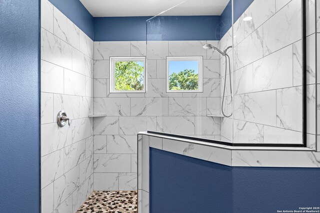 bathroom with a textured wall and tiled shower
