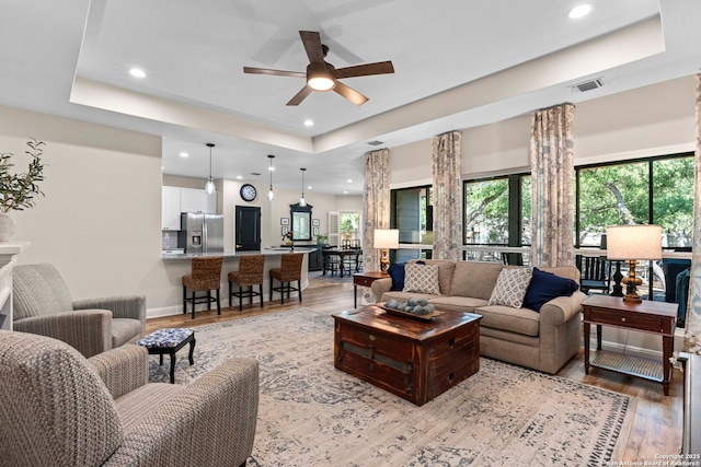 living area featuring recessed lighting, a ceiling fan, a tray ceiling, and light wood-style flooring