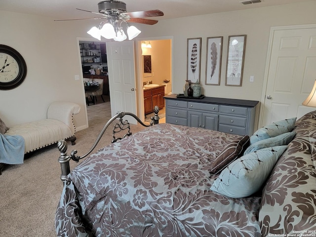 bedroom with visible vents, a ceiling fan, light carpet, a sink, and ensuite bath